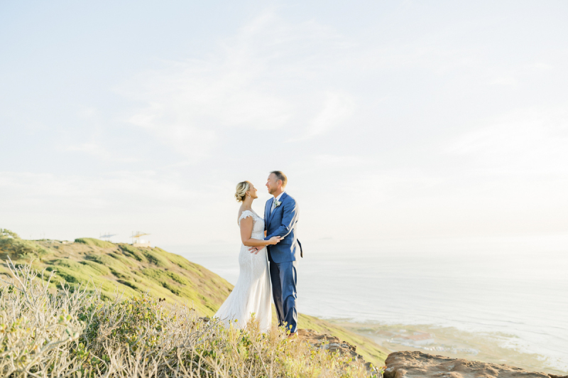 Couple standing on patch of grass near the ocean.