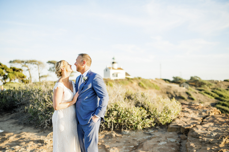 Bride and groom embracing with lighthouse in the background.